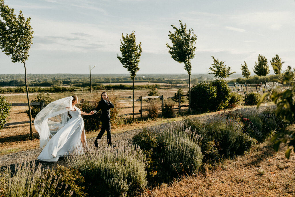 Pár kézen fogva sétál a tanya udvarában, kreatív esküvői fotó