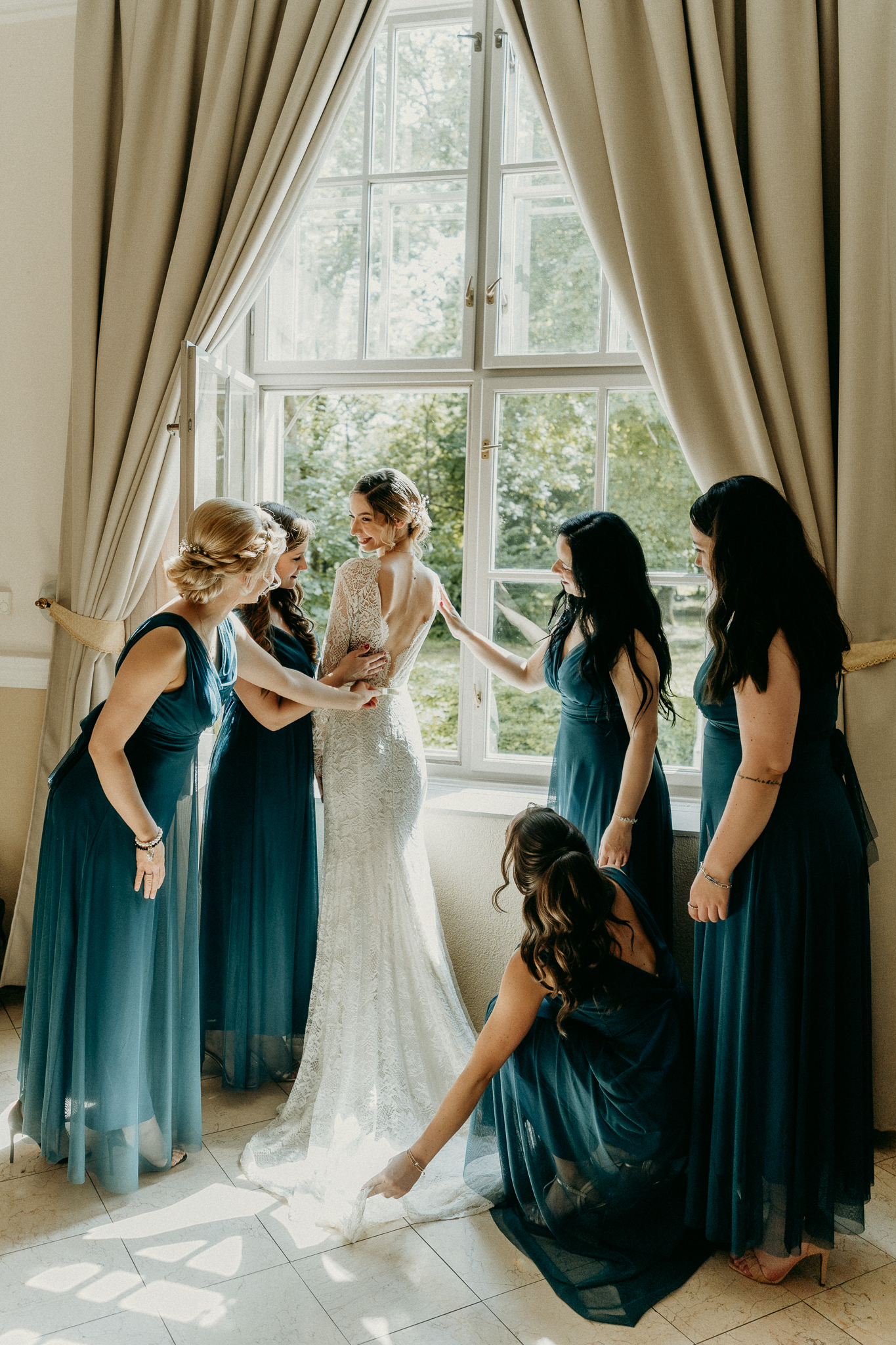 Menyasszony nevetgél koszorúslányaival az esküvői készülődés közben, vidám, elkapott pillanat természetes fényben.