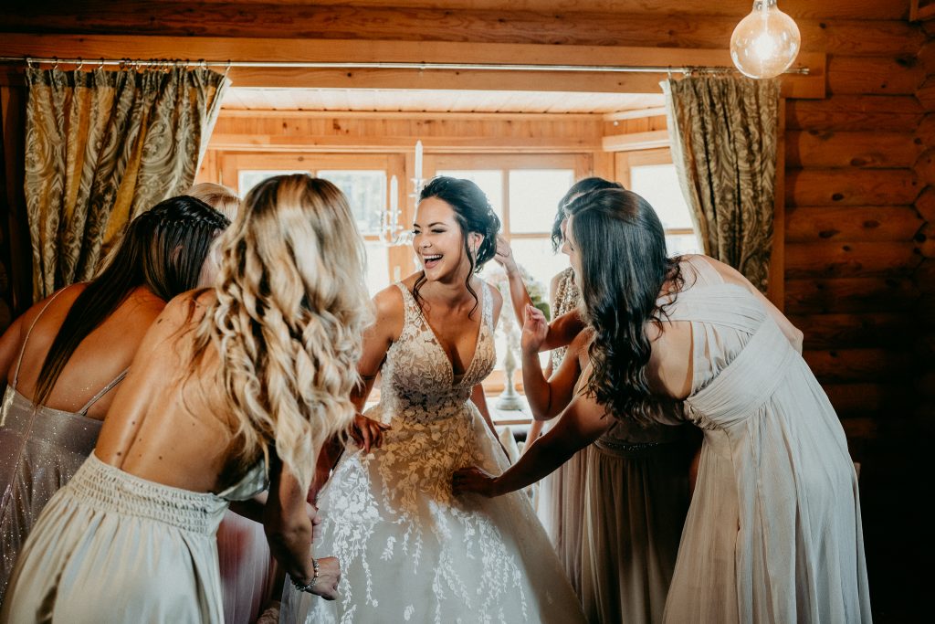 Menyasszony nevetgél koszorúslányaival az esküvői készülődés közben, vidám, elkapott pillanat természetes fényben a wedding morning hangulatában.